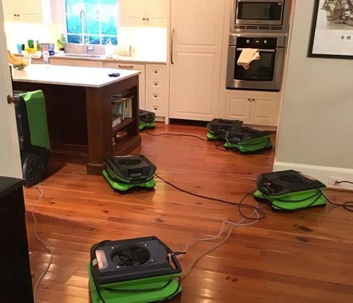 Kitchen with wood flooring has green Servpro air moving equipment placed to restore flooring after a water damage.