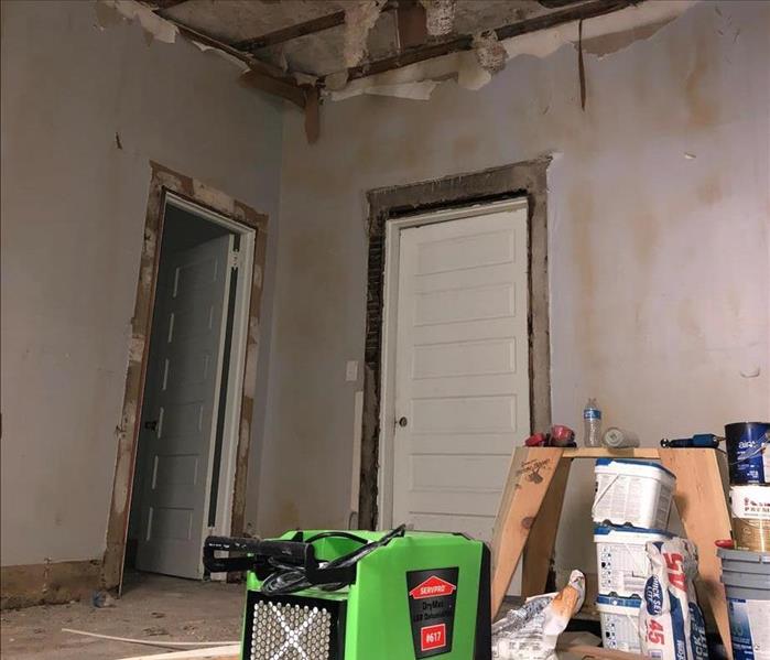 Green SERVPRO dehumifier in a room affected by a fire damage, ceiling is exposed where you can see subfloor
