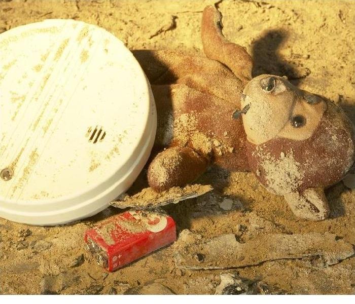 fire damaged smoke alarm with battery out and stuffed animal on floor